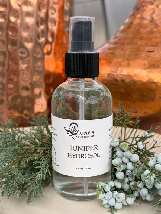 Bottle of Juniper Hydrosol with a label on a surface with greenery.